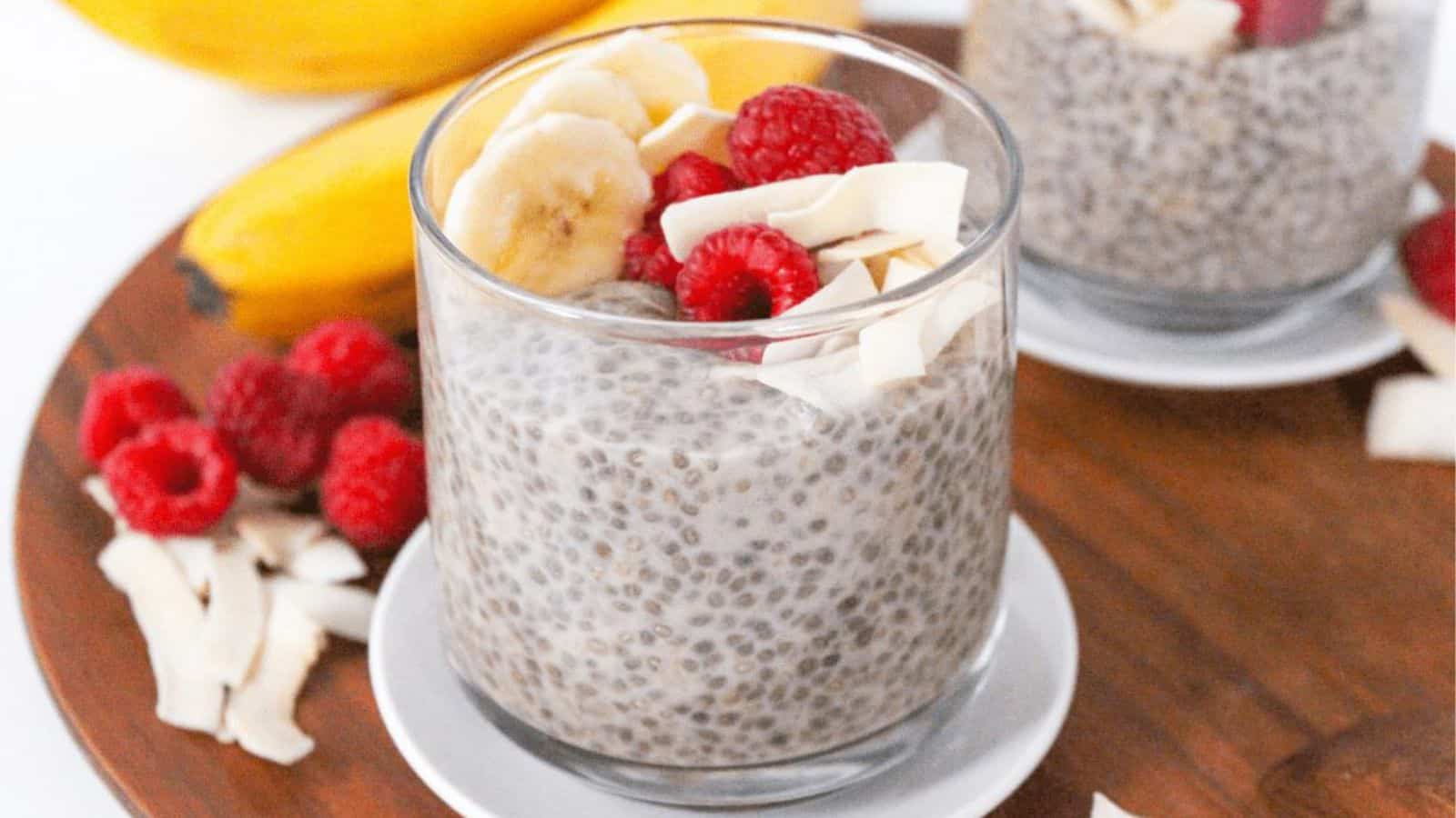 A small glass jar with chia pudding topped with banana slices, coconut flakes, and raspberries.