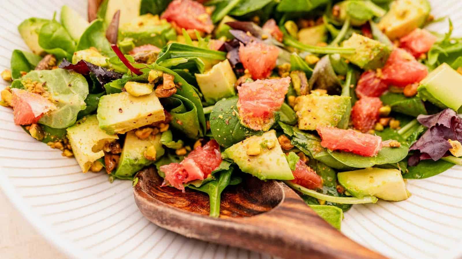 A plate of avocado grapefruit salad with a wooden spoon.