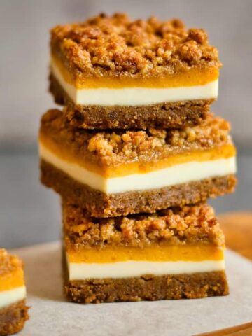 Stack of three pumpkin cheesecake bars on a flat surface.