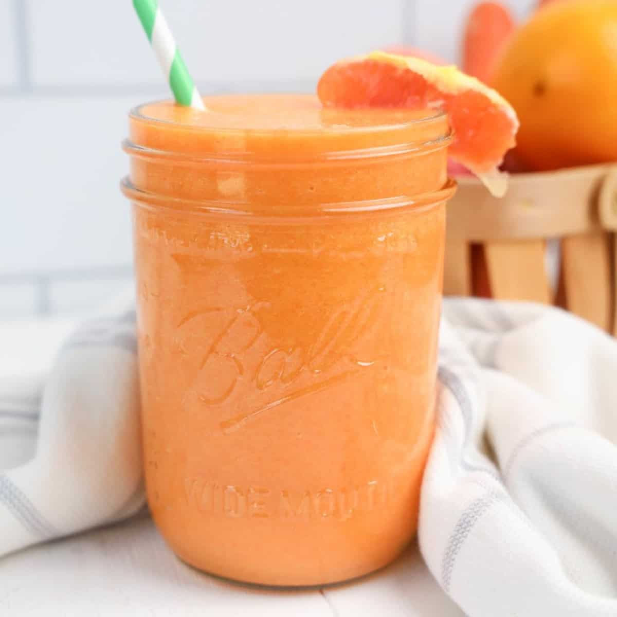 A glass jar with orange juice and a straw.