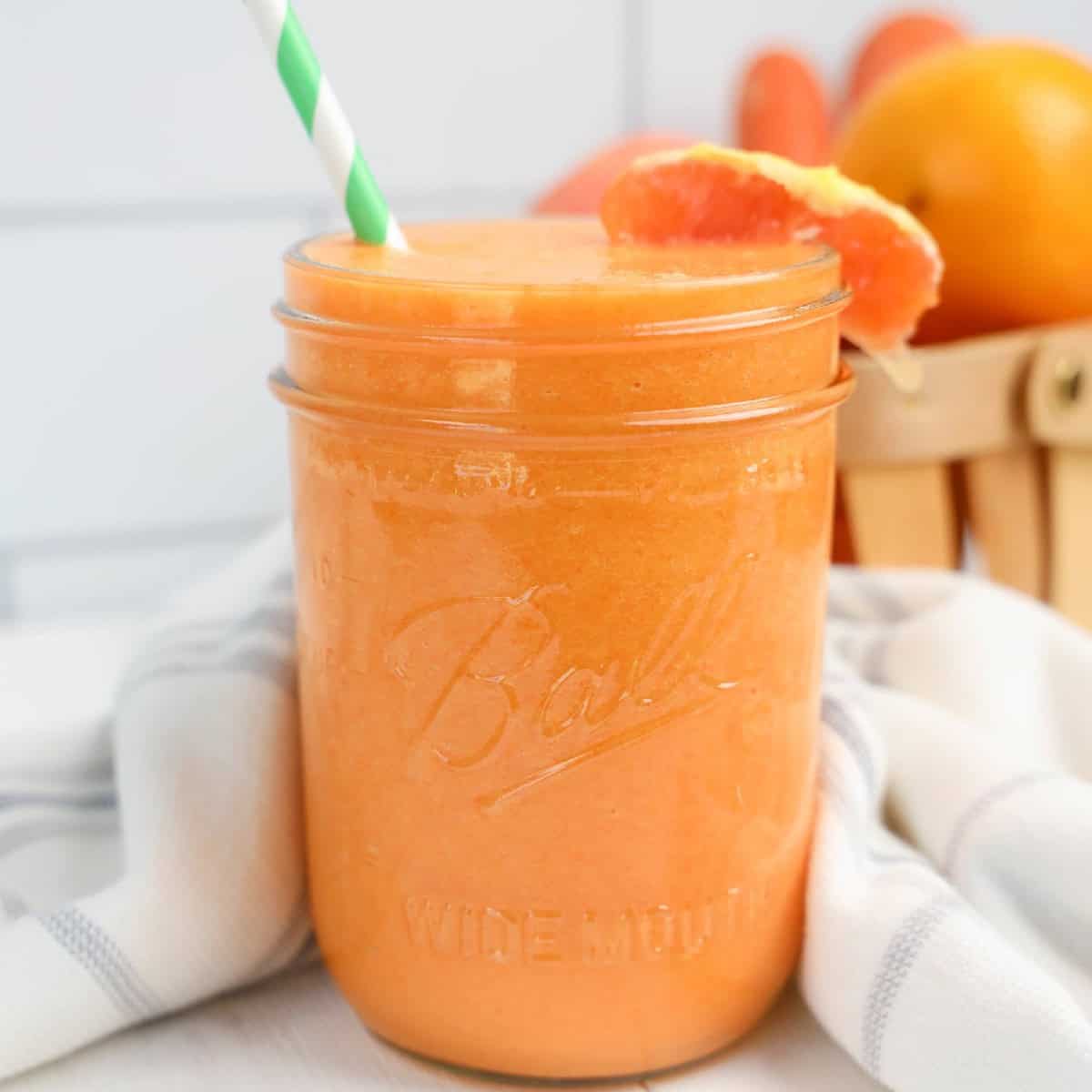 A mason jar filled with orange juice and a striped straw.