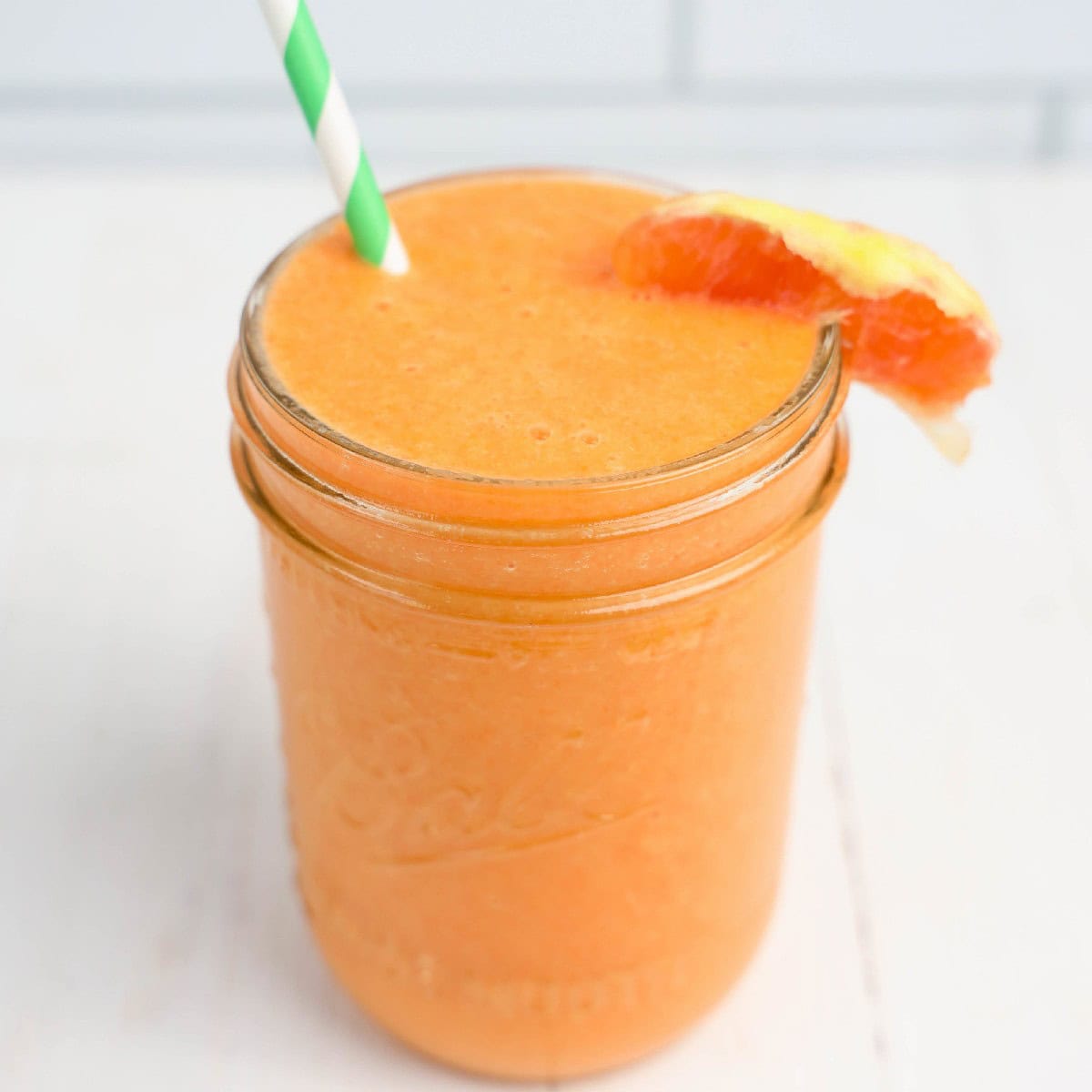 A glass jar filled with orange juice and a straw.
