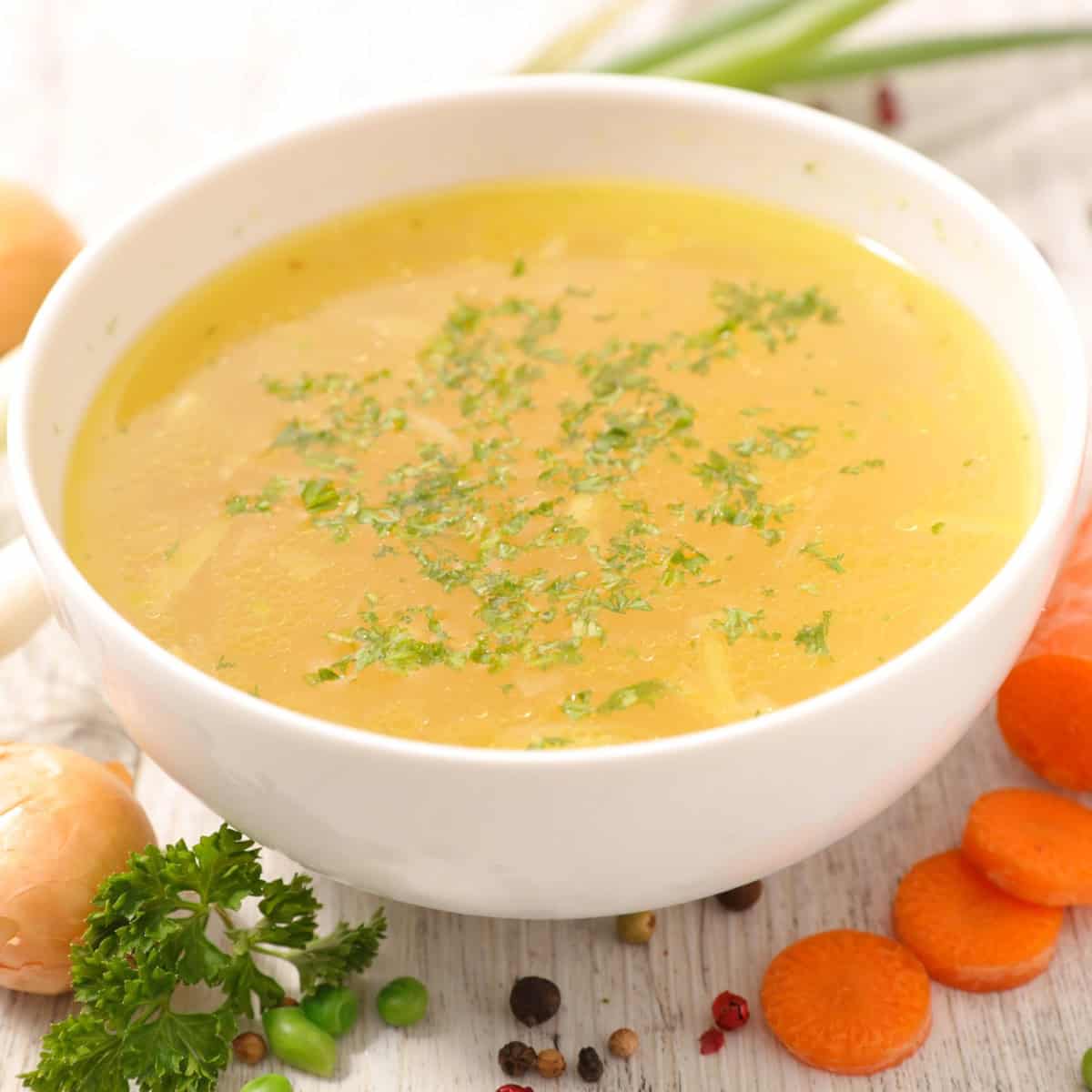 A bowl of soup with carrots, onions and herbs.