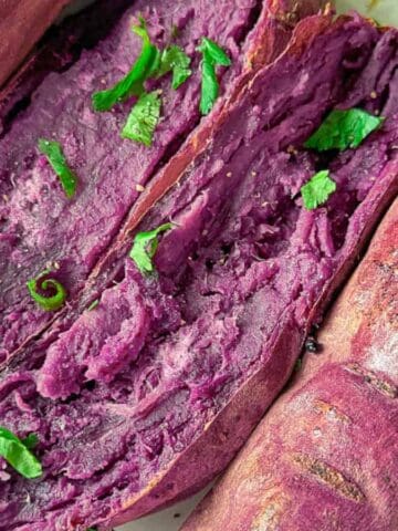 Sweet and creamy oven-roasted purple yams on a white plate with green onions.