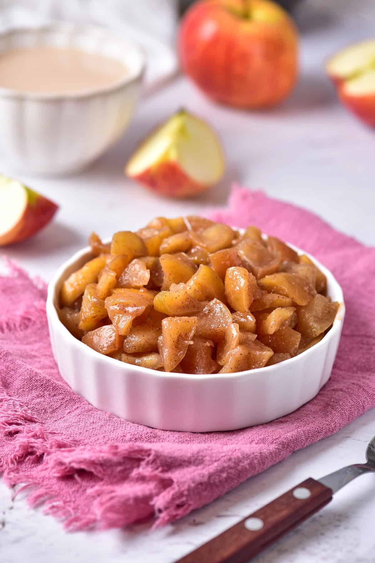 A bowl of cooked apples placed on a soft pink towel.