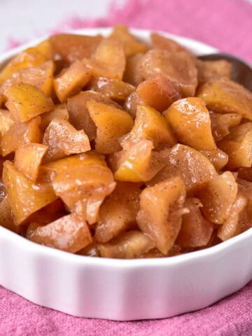 Cooked delicious sweet apples in a bowl, resting on a cozy pink towel.