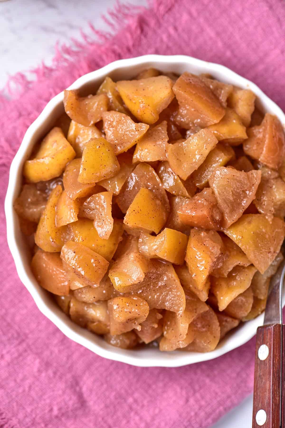 A bowl filled with cooked red apples, set on a light pink towel.