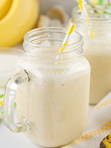 Creamy homemade banana milk in mason jar glasses with yellow striped straws.