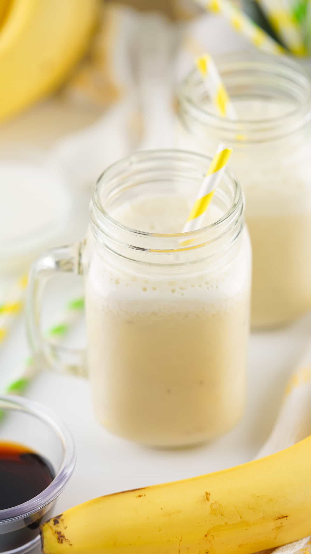 Glass of banana milk with vanilla extract and ripe banana in the foreground, perfect for a healthy drink.