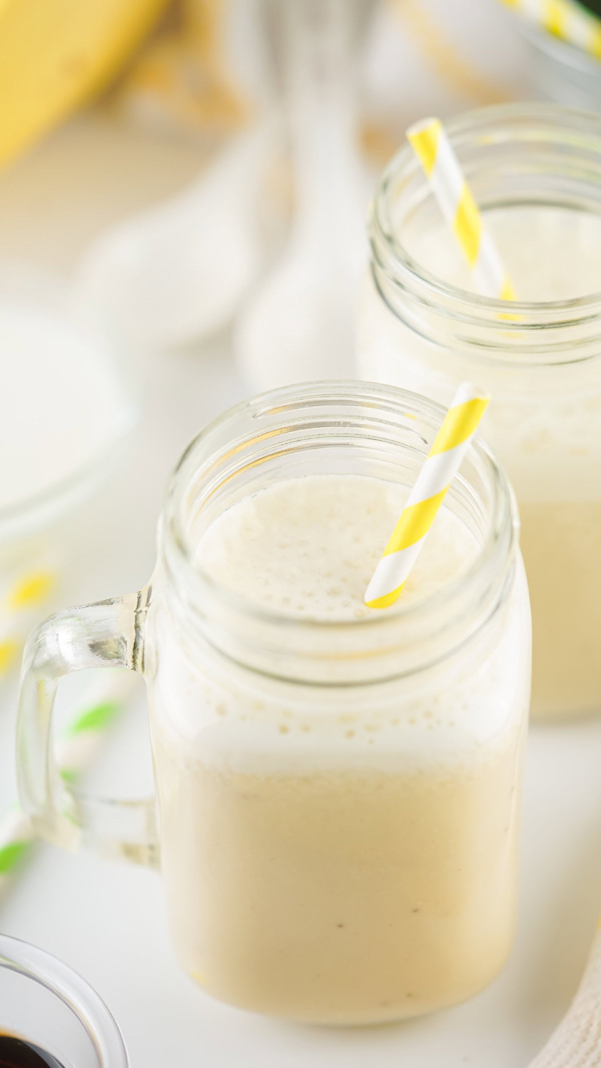 Close-up view of banana milk foam in a mason jar with a yellow-striped straw, showcasing creamy texture.