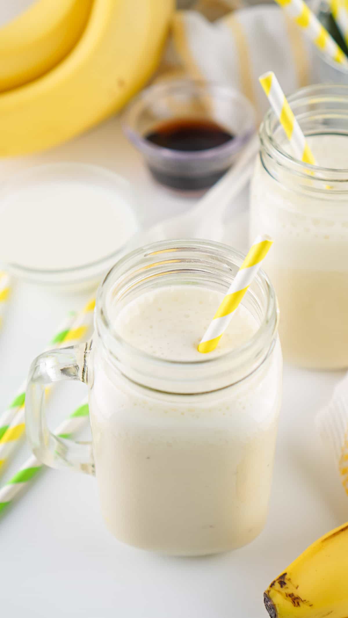Banana milk in glass jars with bananas, milk, and vanilla extract in the background.