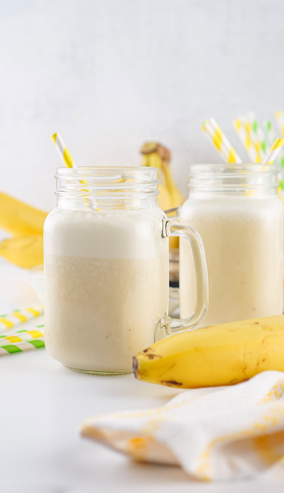 Two mason jars filled with creamy banana milk and striped paper straws, served chilled.