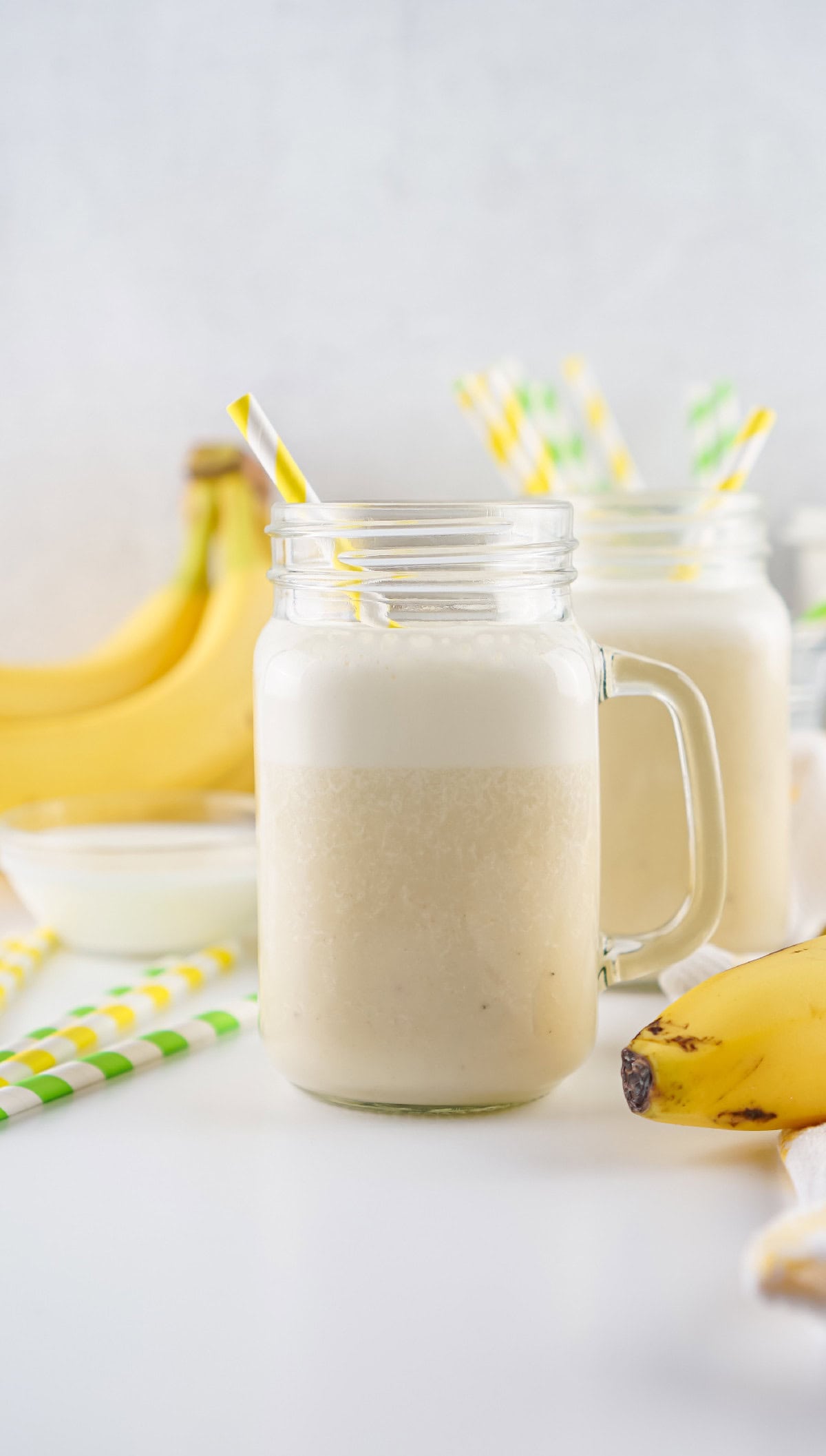Freshly blended banana milk in a mason jar with a yellow-striped straw, ready to drink.