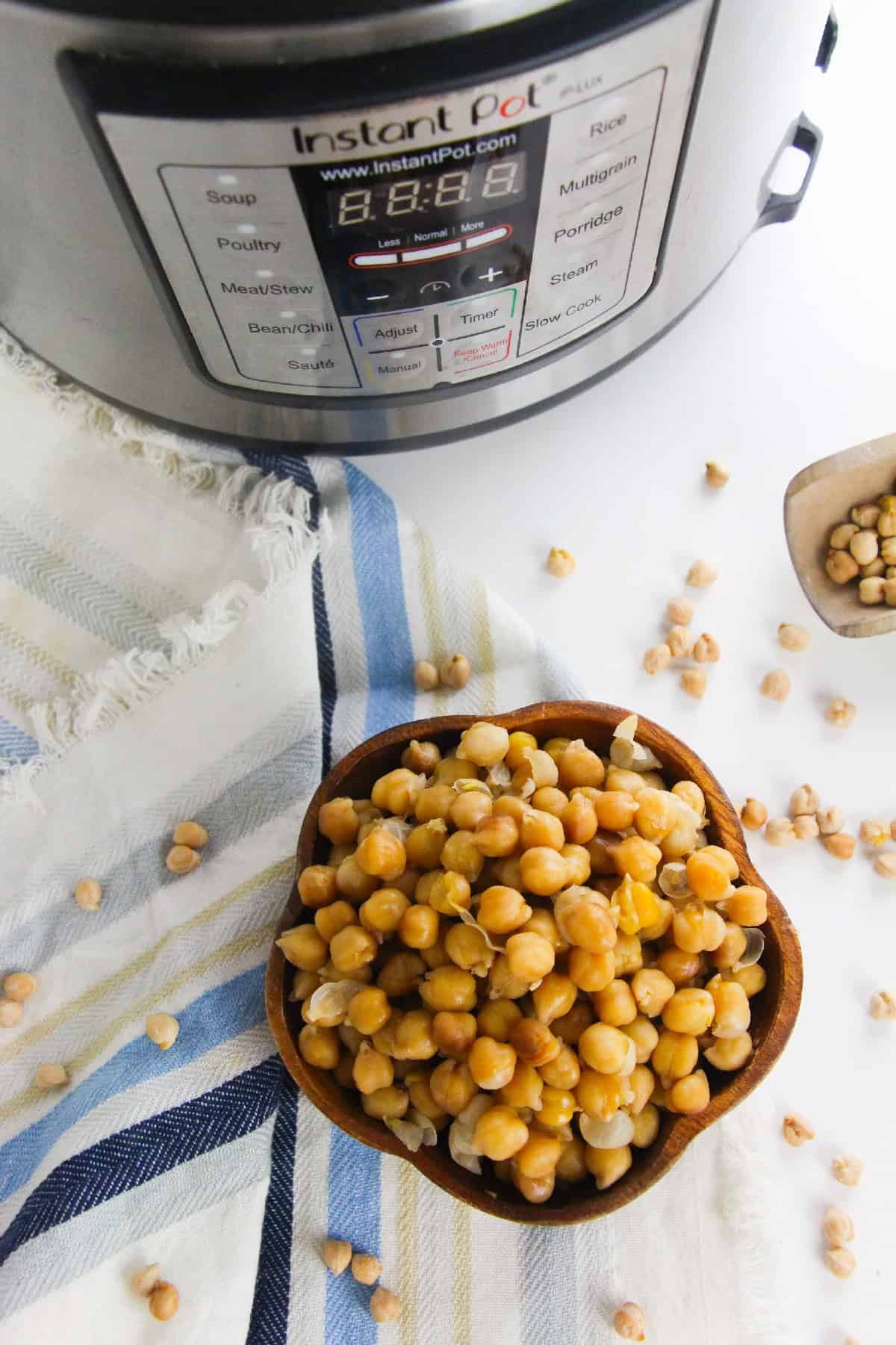Cooked chickpeas in a brown wooden bowl placed in front of an silver Instant Pot.
