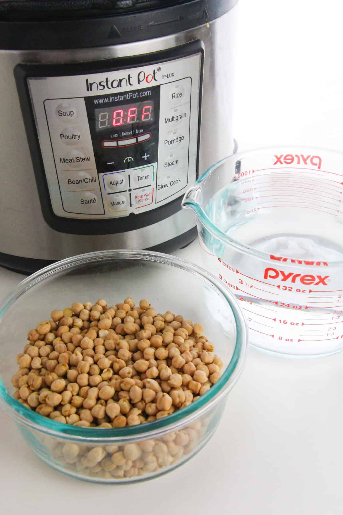 Ingredients for cooking dried chickpeas in an Instant Pot, including a bowl of chickpeas, water in a measuring cup, and a pressure cooker.