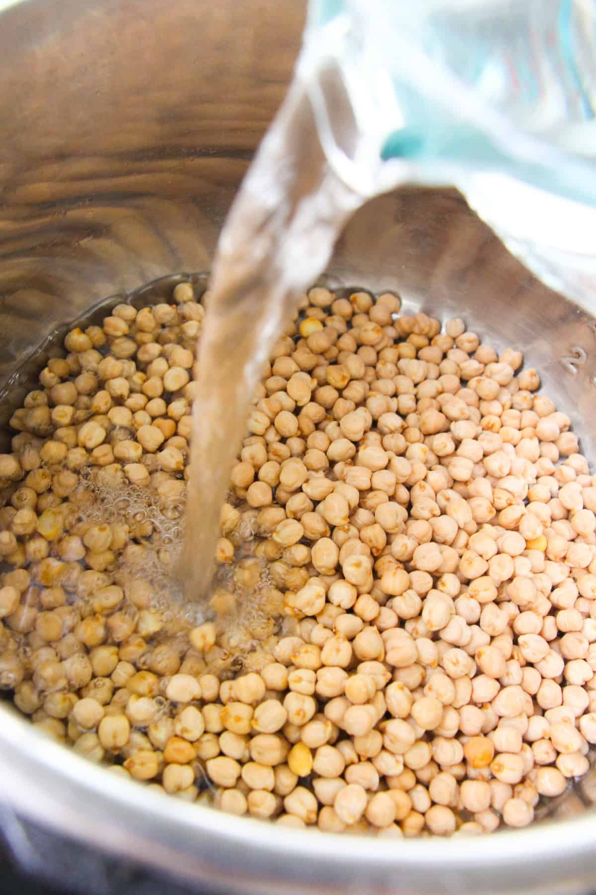 Pouring water over dried chickpeas in an Instant Pot for pressure cooking.