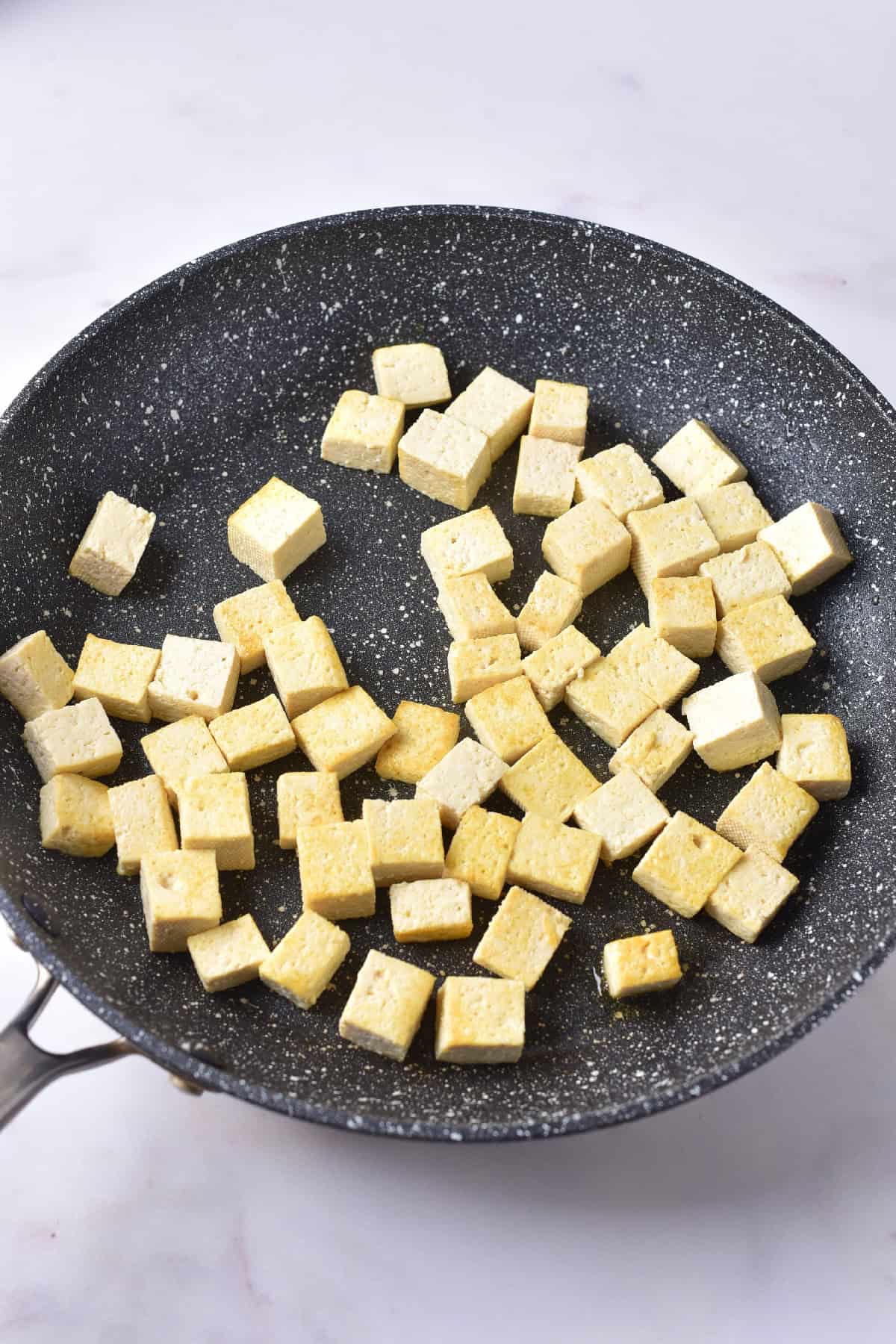 Cubed tofu pieces cooking in a nonstick skillet, lightly browned for a yellow tofu curry dish.