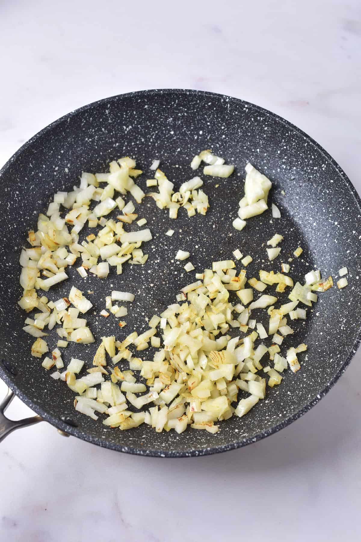 Finely chopped onions sautéing in a skillet until lightly golden, forming the flavor base for tofu curry.