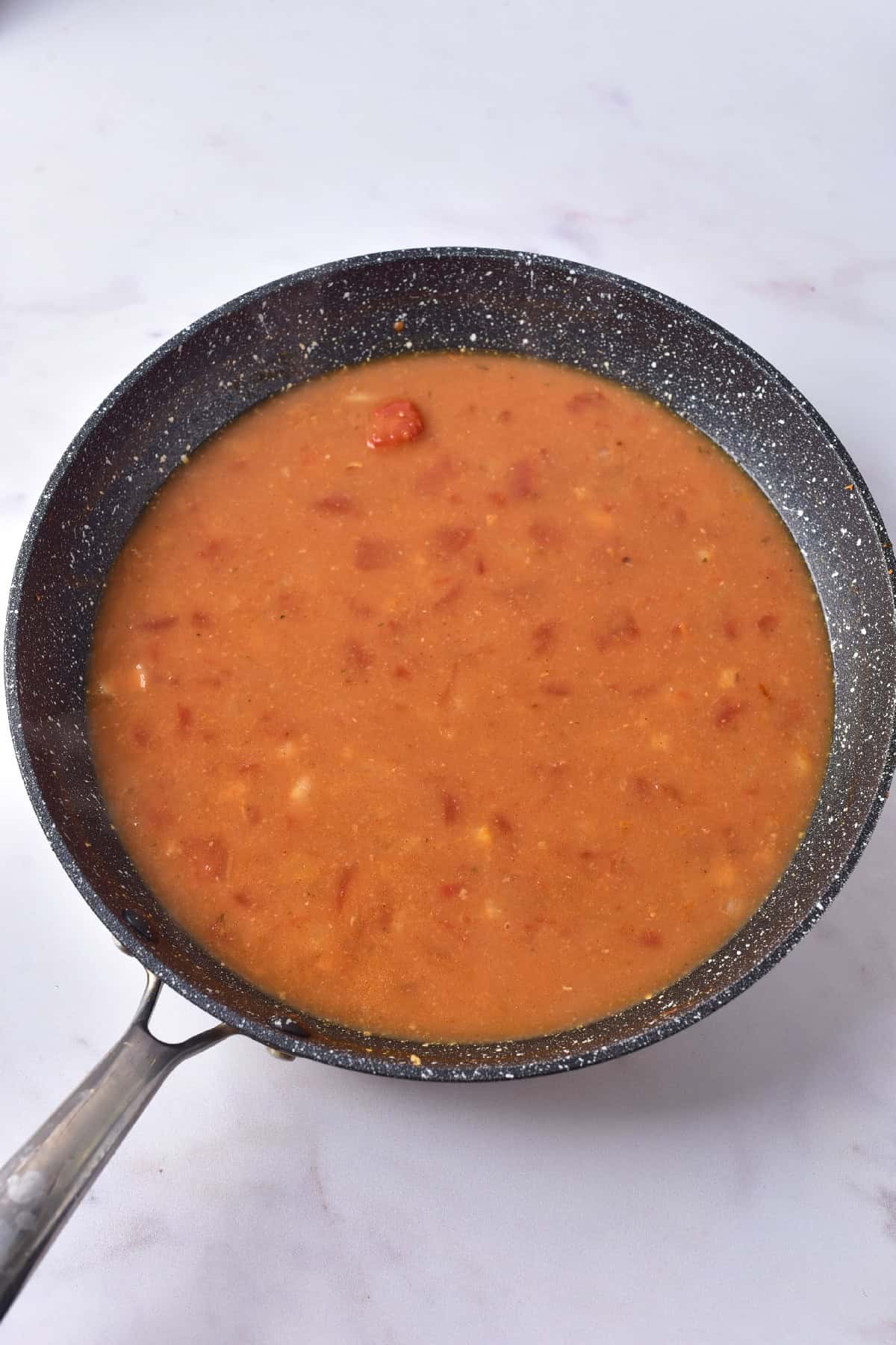 Coconut milk and tomato curry sauce simmering in a skillet, ready to be combined with tofu.