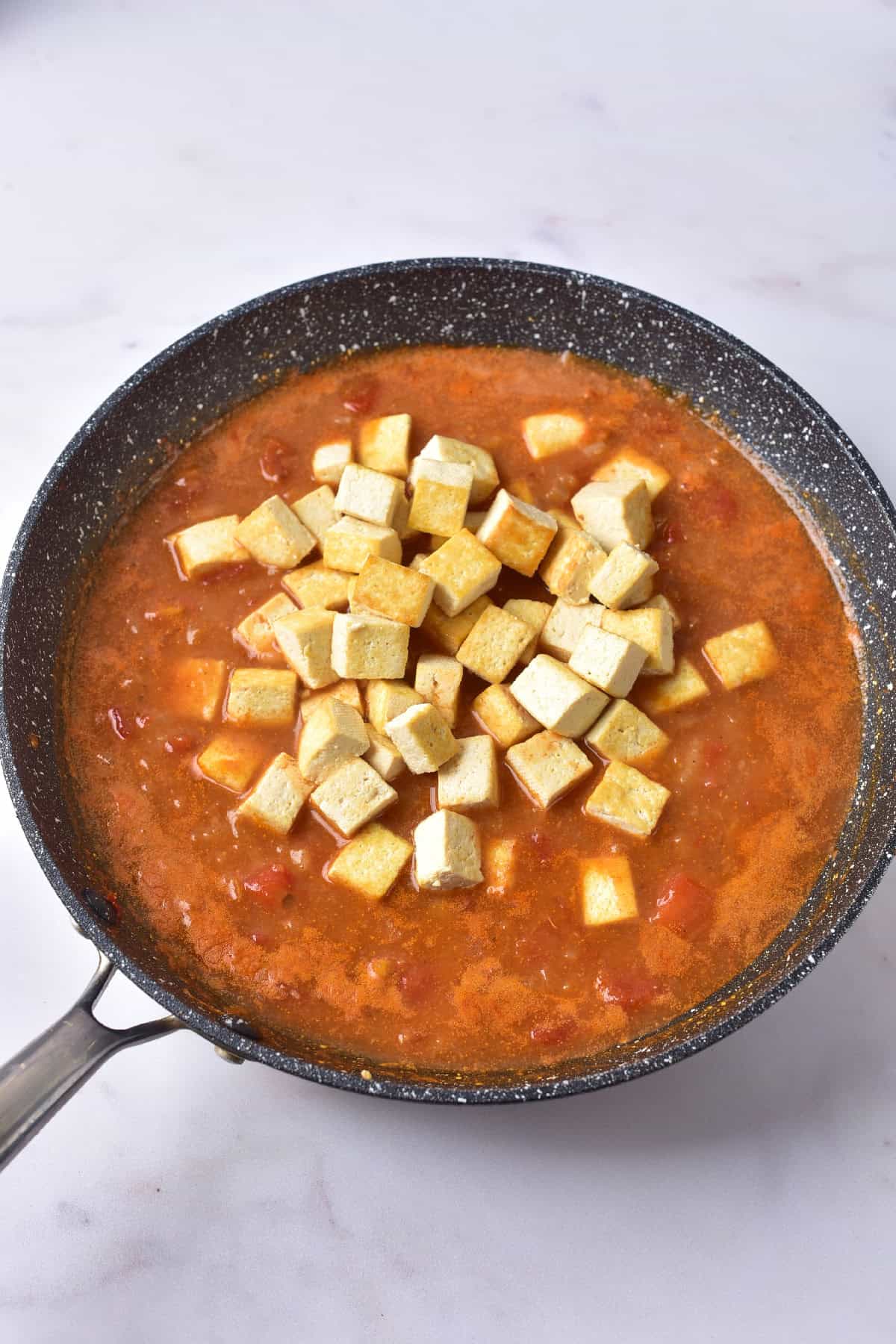 Crispy tofu cubes added to a rich coconut tomato curry sauce in a pan, preparing for final simmer.