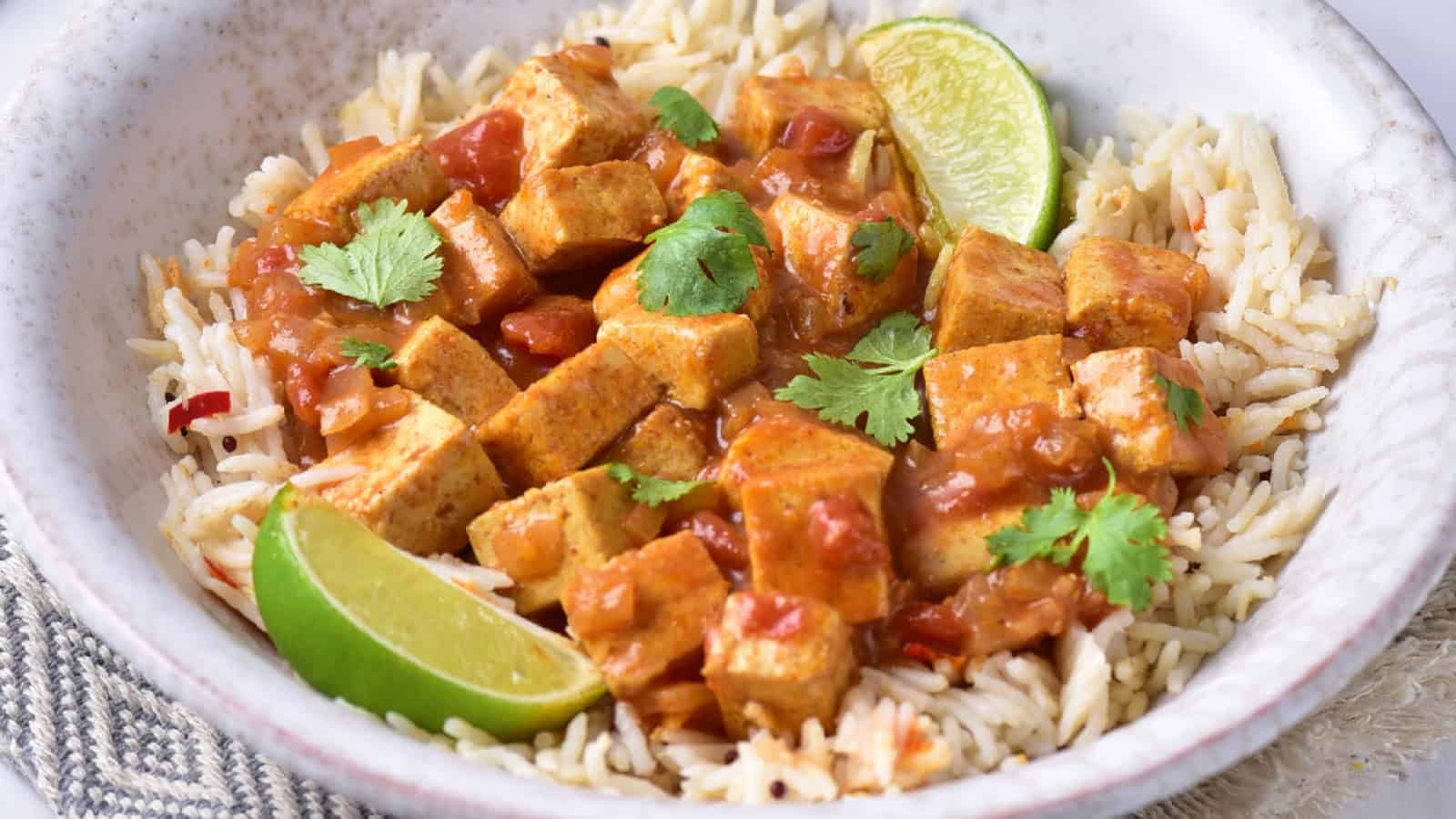 Bowl of yellow tofu curry made with coconut milk, garnished with fresh herbs and served with rice.