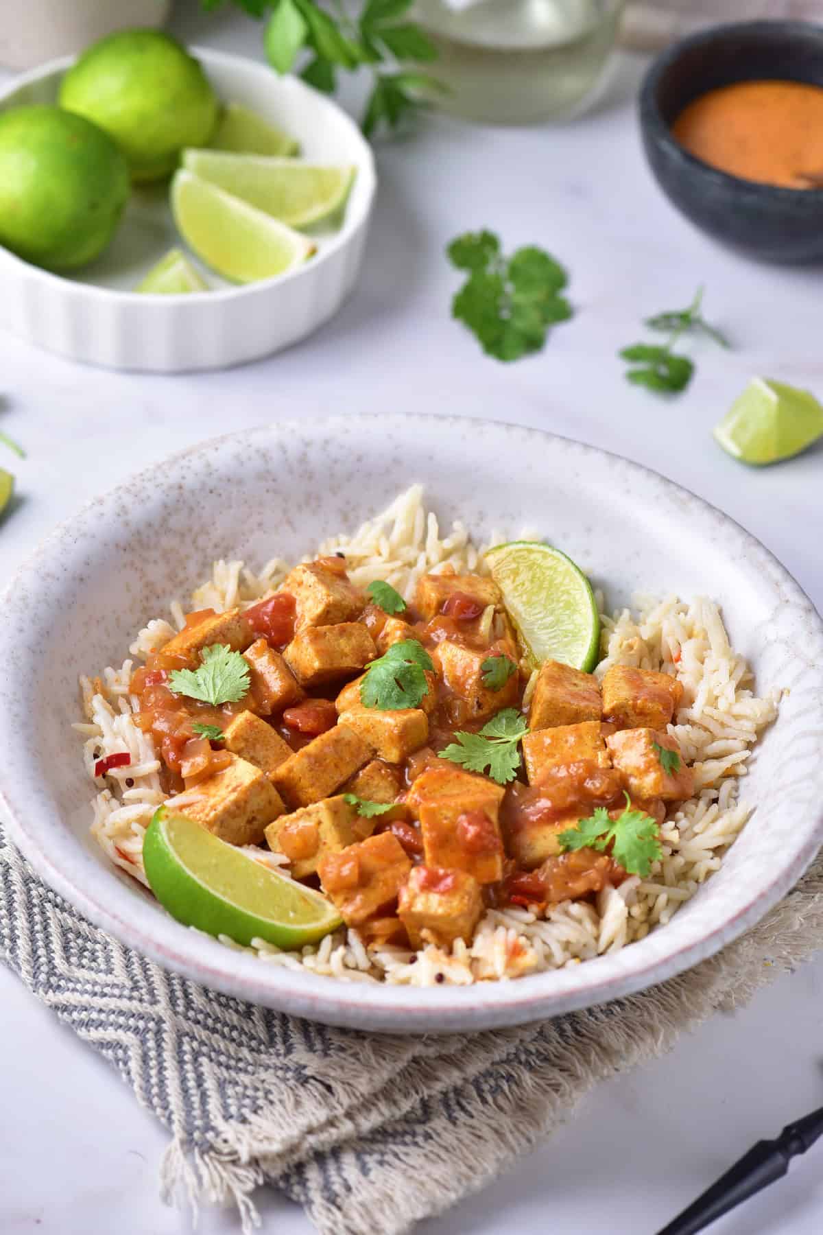 Finished yellow tofu curry served over rice in a ceramic bowl, garnished with fresh cilantro and lime wedges.