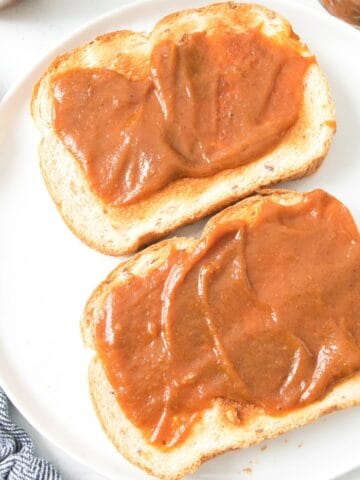 Pumpkin butter spread on toast with jars and a knife in the background.