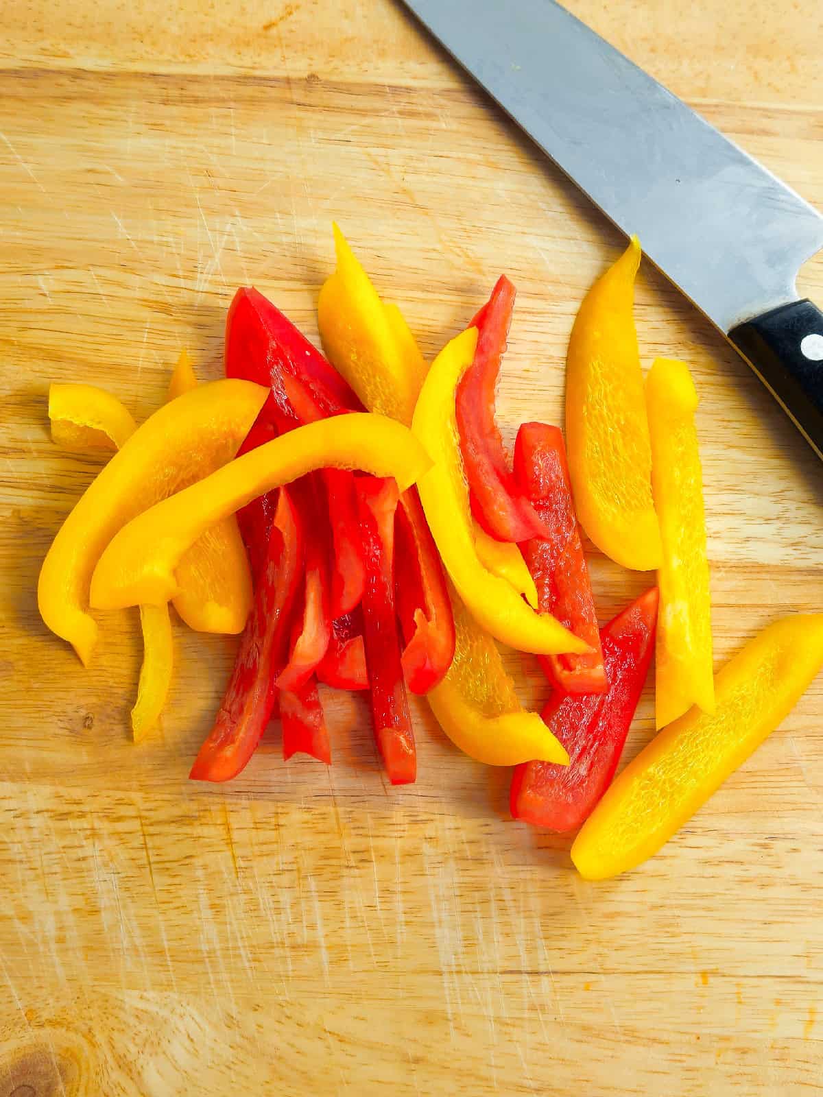 Fresh red and yellow bell pepper strips on a wooden cutting board, ready for cooking.