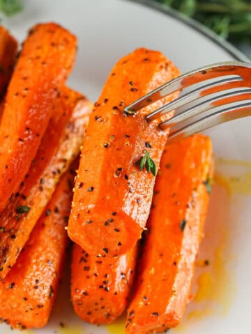Fork lifting a roasted air fryer carrot from a plate of herb-seasoned carrots.