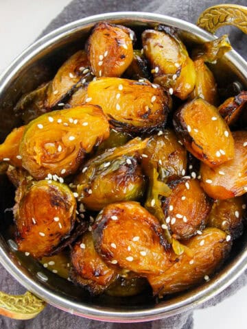 Crispy air-fried Korean Brussels sprouts glazed with gochujang sauce and sprinkled with sesame seeds, served in a metal bowl.