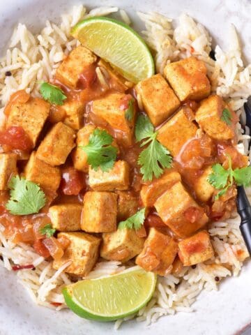 Flat lay of tofu curry with long-grain rice and lime, highlighting vibrant curry sauce.