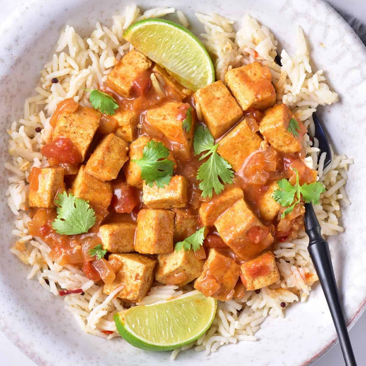 Flat lay of tofu curry with long-grain rice and lime, highlighting vibrant curry sauce.