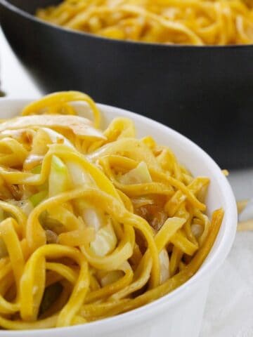 Cooked chow mein noodles with cabbage and onions in a wok and bowl.