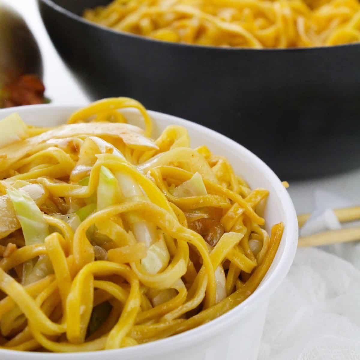 Cooked chow mein noodles with cabbage and onions in a wok and bowl.