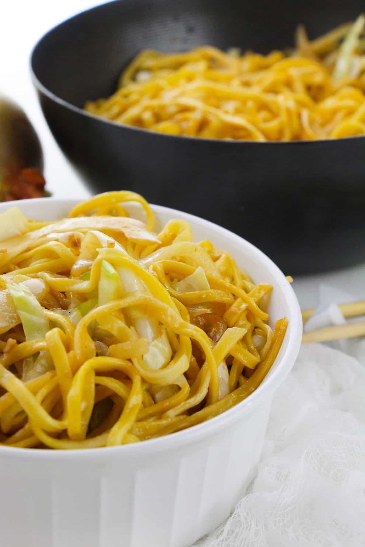 Freshly cooked chow mein noodles with cabbage and onions in a wok and bowl.