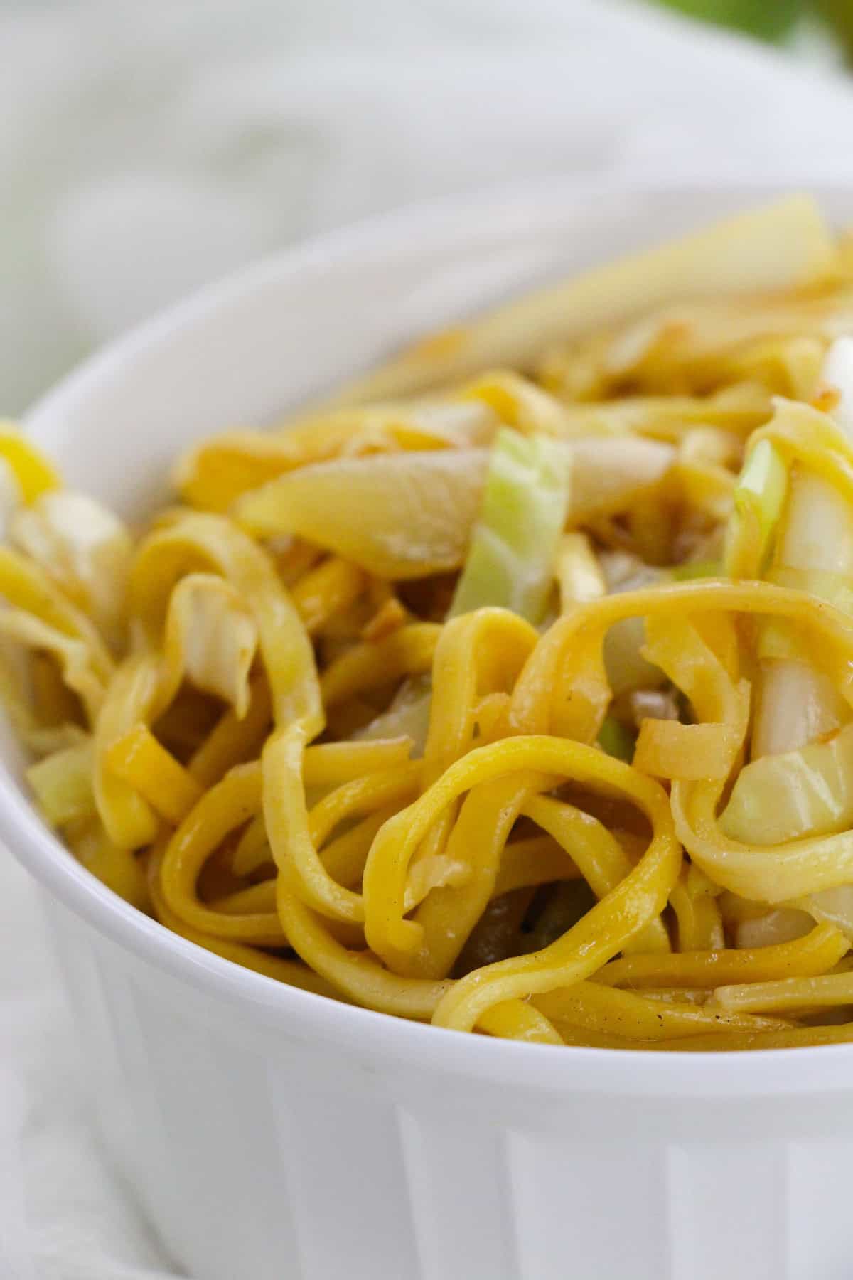 White bowl of stir-fried chow mein noodles with cabbage and soy sauce.