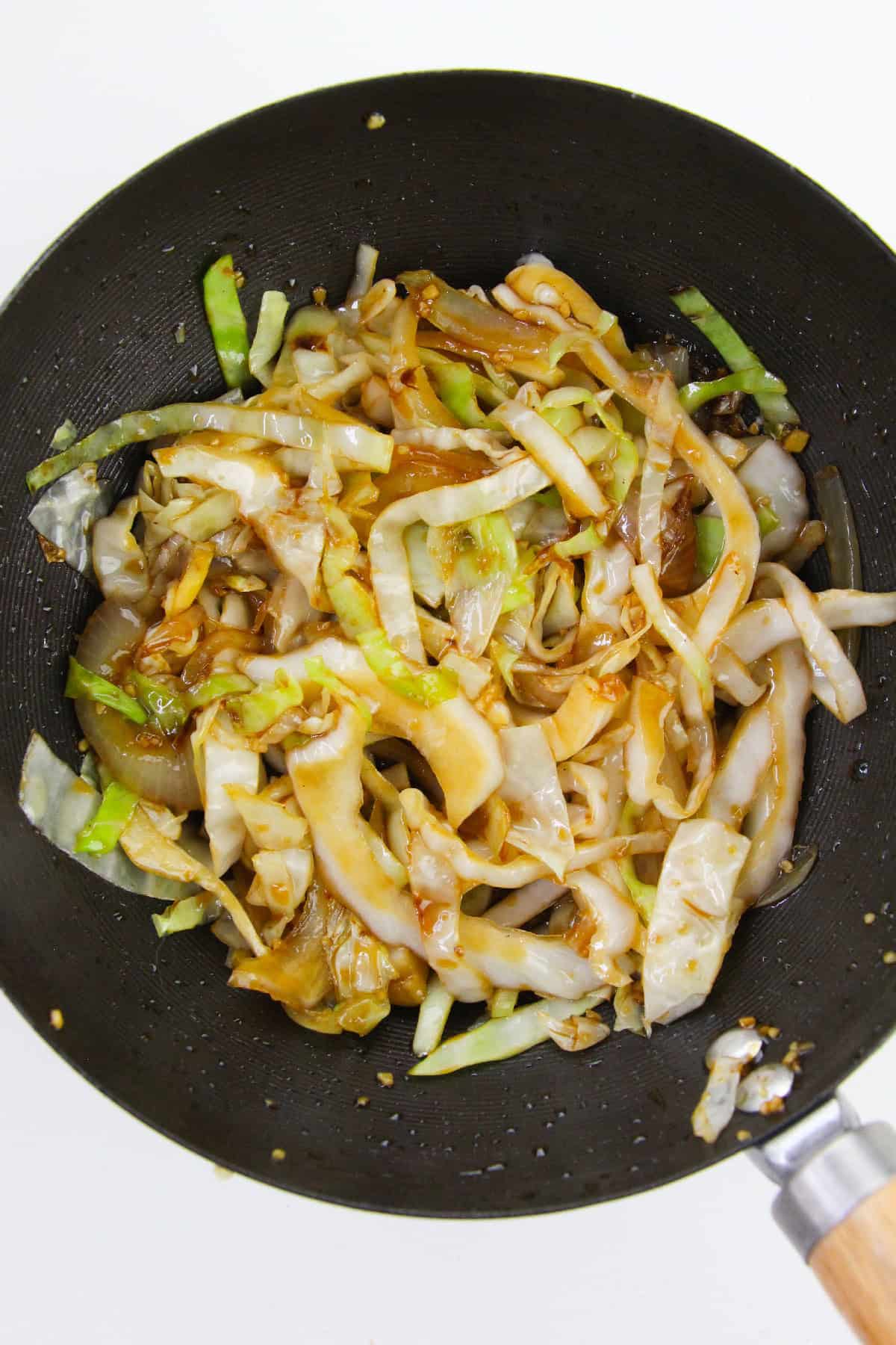 Cabbage and onions coated in savory sauce while stir-frying in wok.