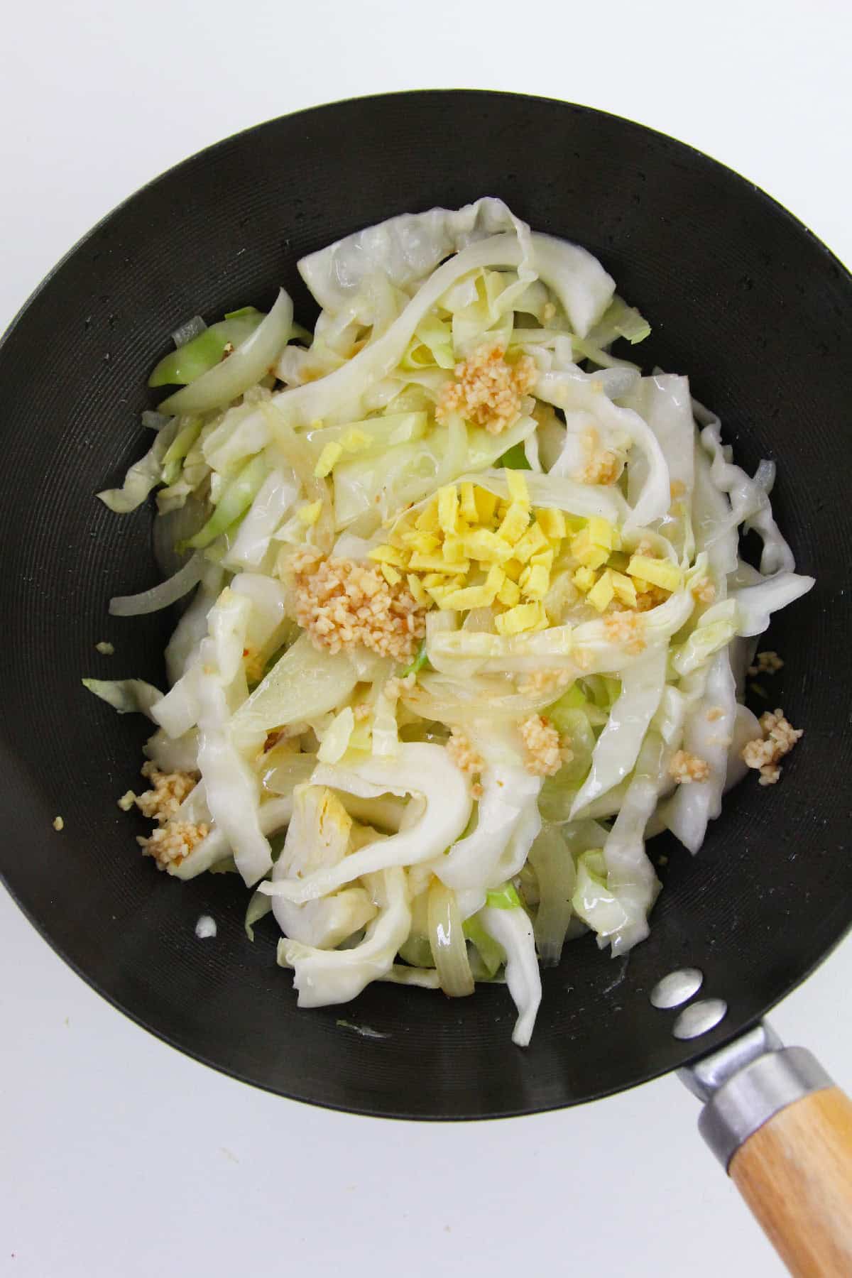 Stir-frying cabbage with minced garlic and chopped ginger in a wok.