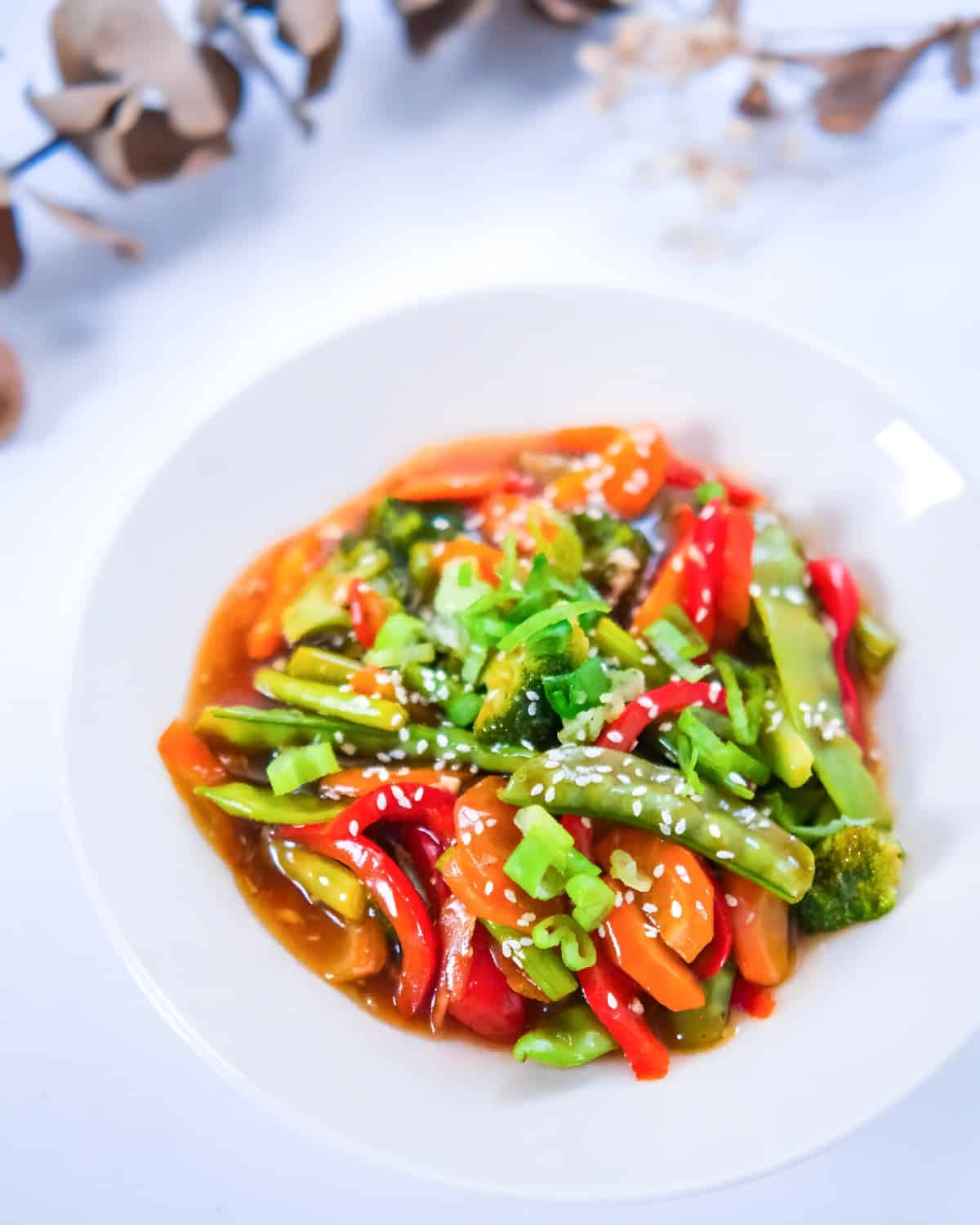 Veggie teriyaki stir fry with broccoli florets, bell peppers, carrots, and snap peas in a glossy sauce, sprinkled with sesame seeds.