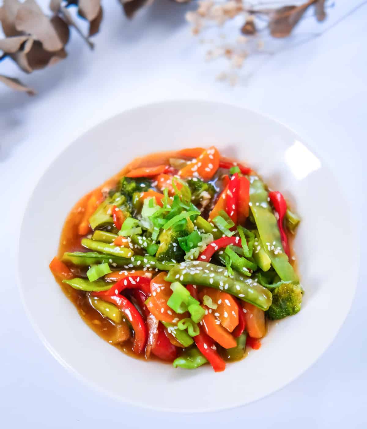 Colorful teriyaki stir fry vegetables in a white bowl, topped with sesame seeds and scallions for garnish.