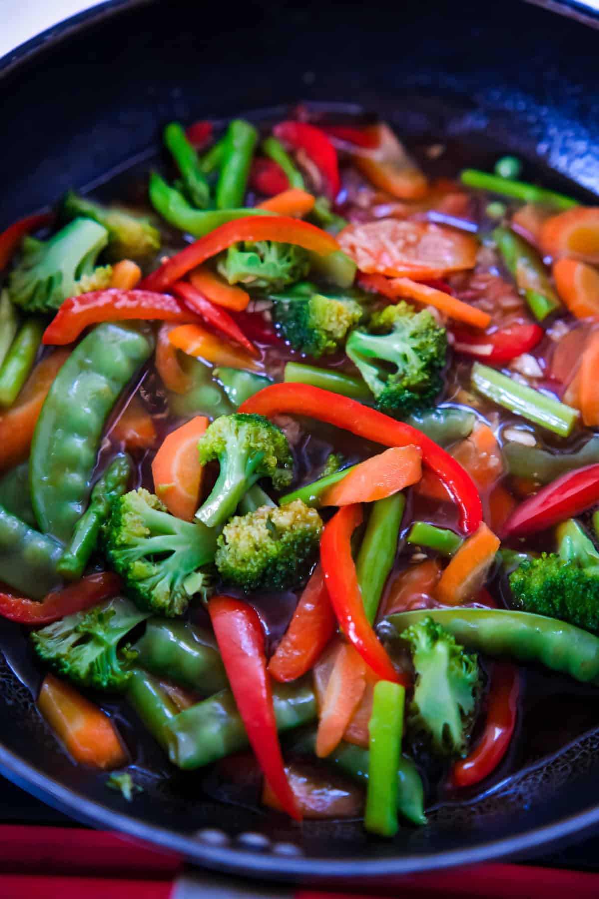 Colorful stir-fry vegetables simmering in a savory teriyaki sauce inside a black skillet.