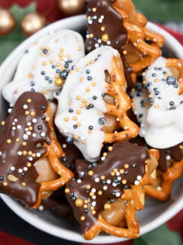 Bowl of New Year’s Eve dipped caramel pretzels shaped like holiday trees, covered in white and dark chocolate with festive gold and silver sprinkles.