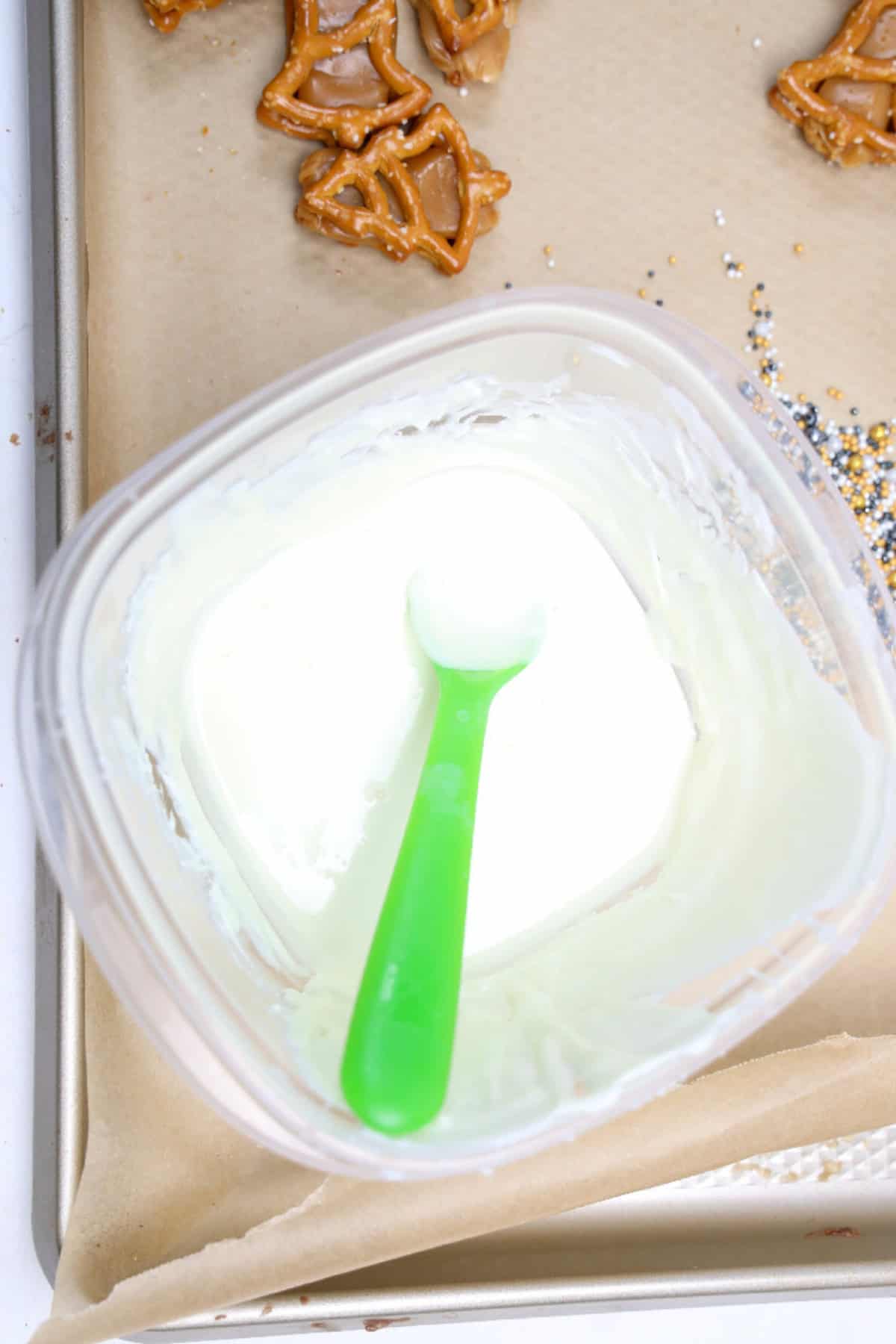 Bowl of melted white chocolate with a green spoon ready for dipping pretzels.