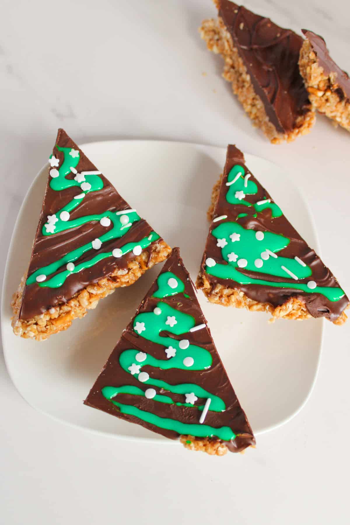 Triangle shaped chocolate peanut butter Christmas tree bars topped with green icing and white sprinkles.