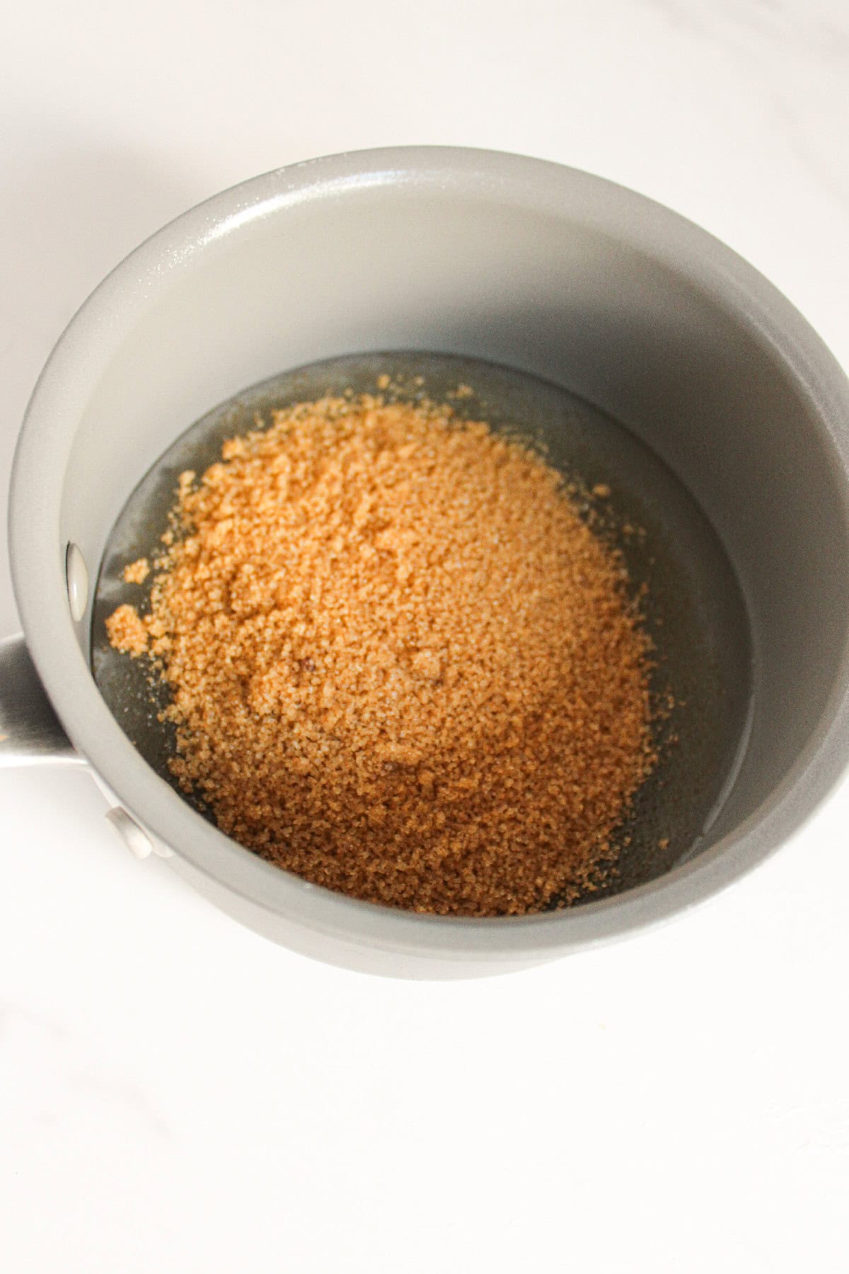 Brown sugar heating in a saucepan with liquid to dissolve.