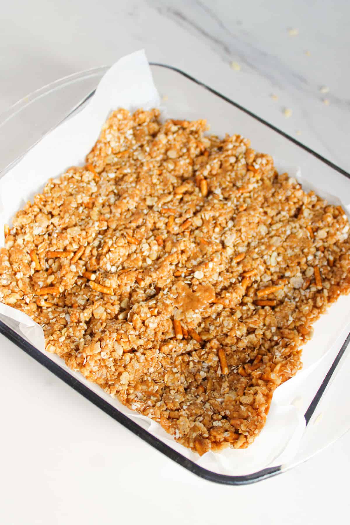 Peanut butter cereal mixture pressed evenly into a parchment lined baking dish.