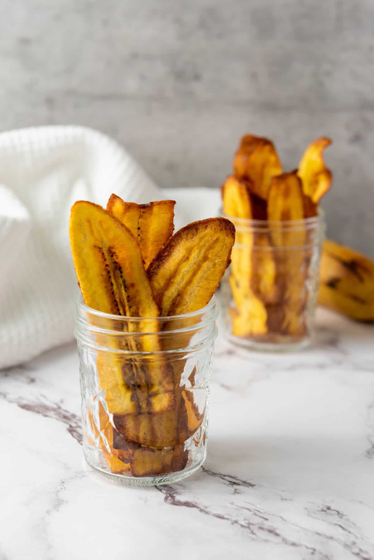 Homemade chifles plantain chips standing upright in a glass jar.