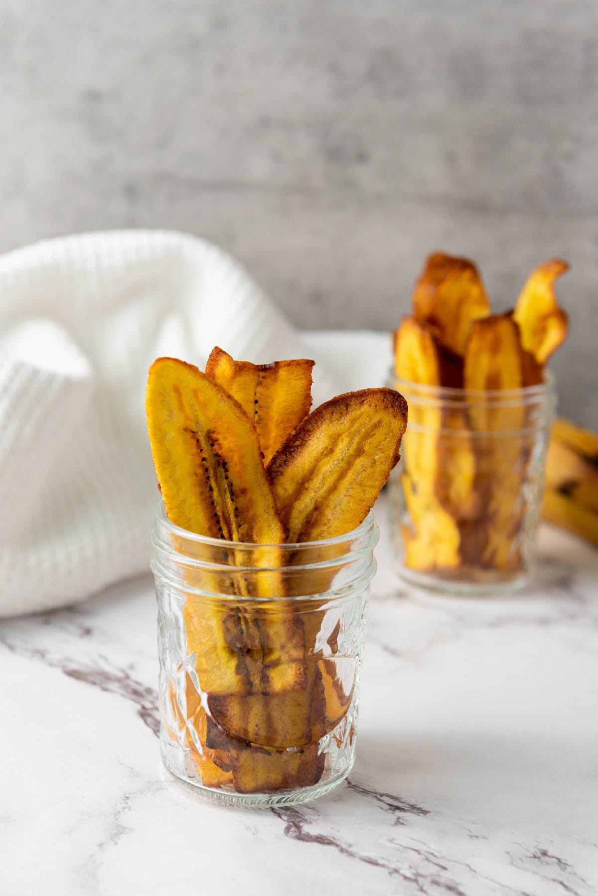 Golden fried chifles plantain chips displayed in a small glass jar.