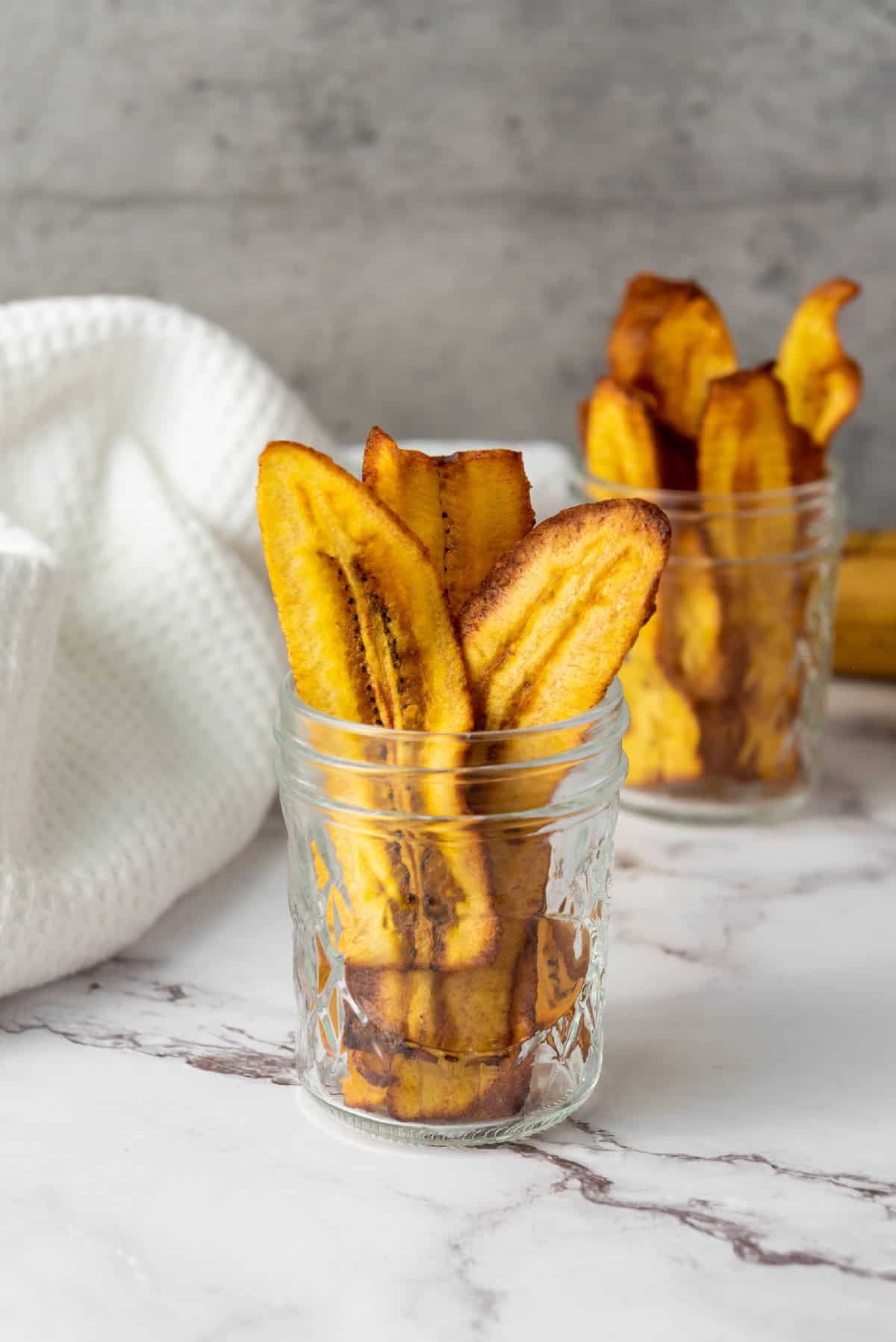 Crispy homemade chifles plantain chips with golden edges in a glass jar.