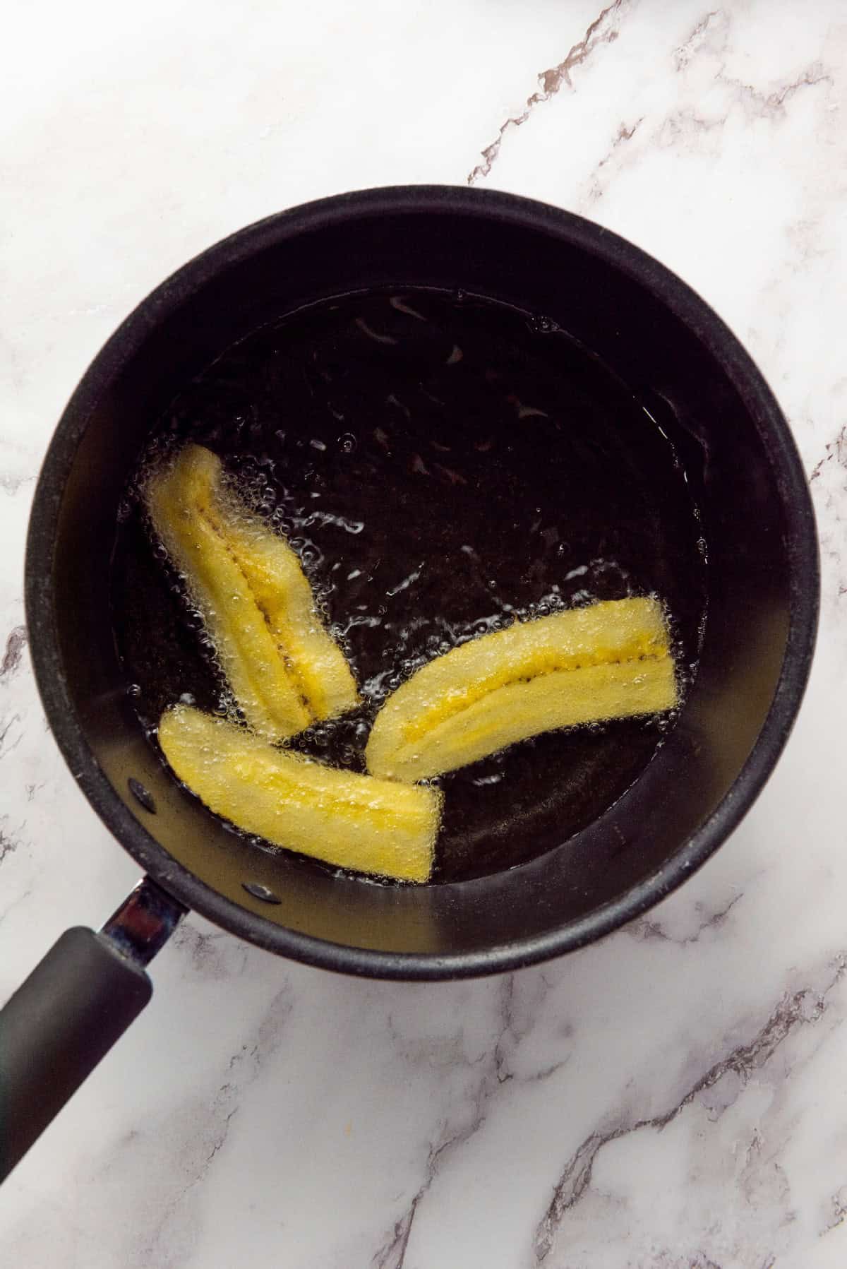 Sliced plantains cooking in oil to make chifles plantain chips.